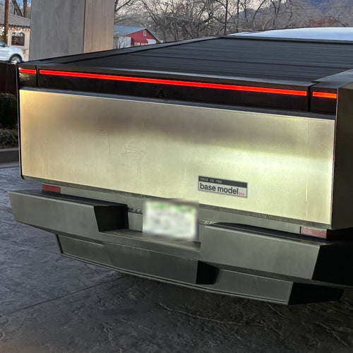 This Is the Base Model btw 11x3 bumper sticker shown on the tailgate of an electric pickup